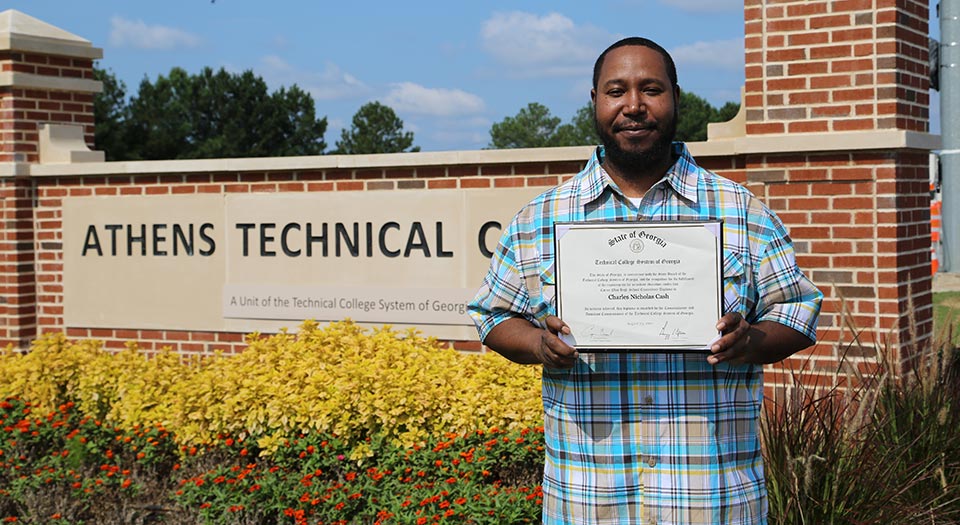 Alumni w/ Degree at front gate of campus