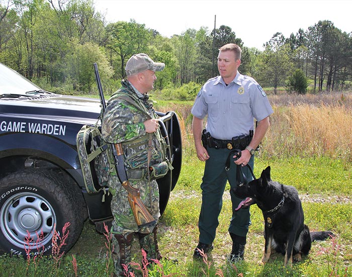 Game warden and police dog outside with armed camo man