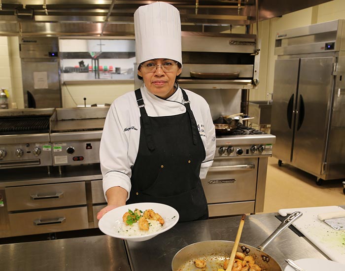 Female Culinary Arts student presenting a plate of shrimp and rice