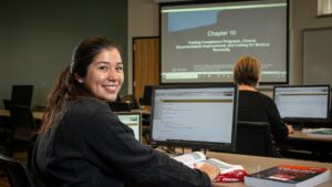 student smiling from desk in a computer lab
