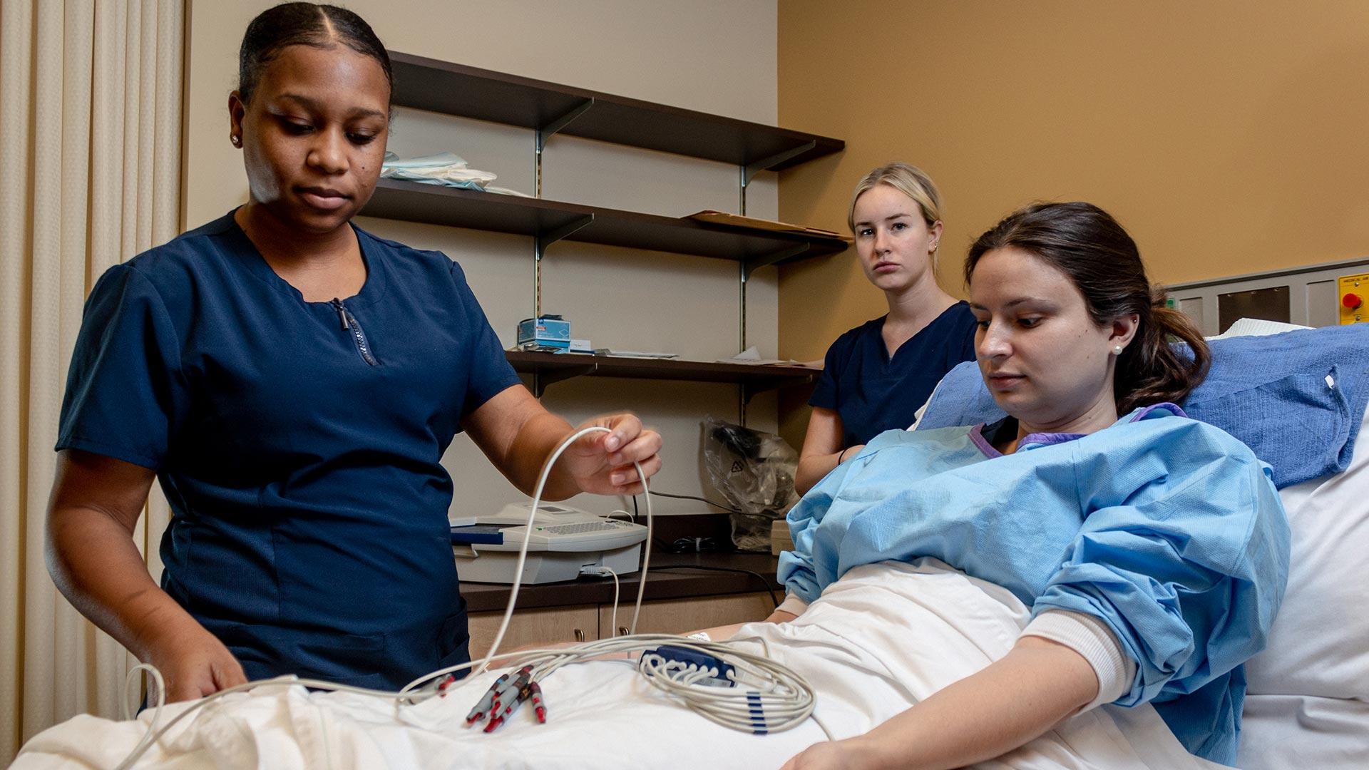 2 Female healthcare assistant students checking vitals of another female student in hospital bed