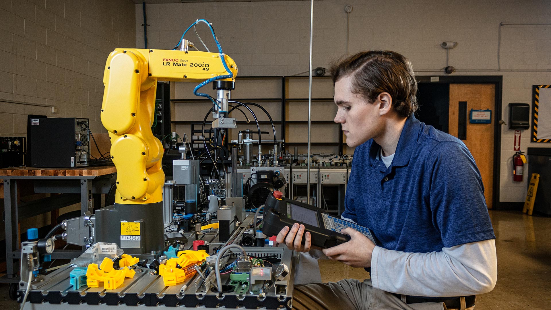 Male student holding device and sitting at an operation machine - manufacturing operations