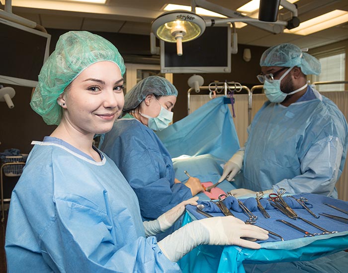 Female student looking at camera other students operating on a dummy - surgical technology