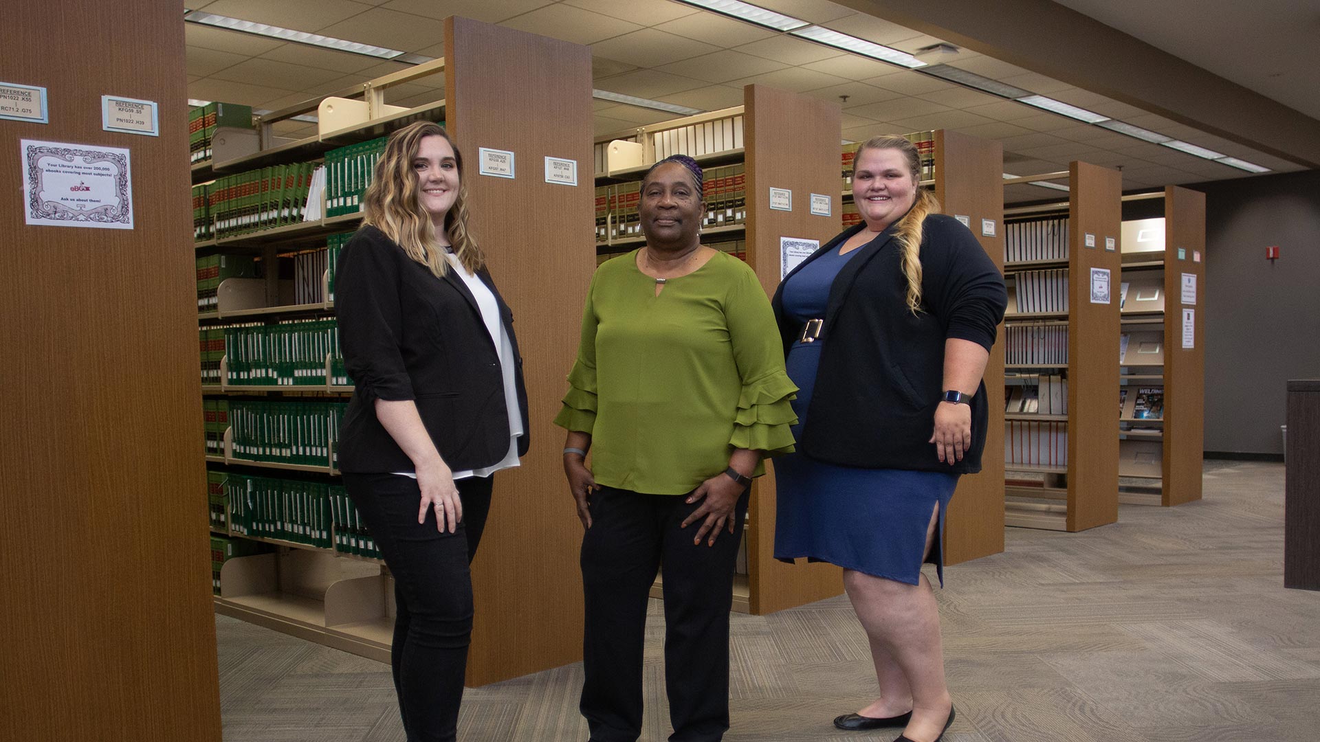 3 Females standing in front of book shelves - paralegal studies