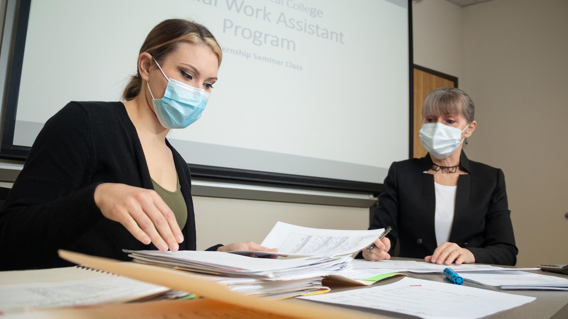 2 females working at desk, social work assistant program on projector